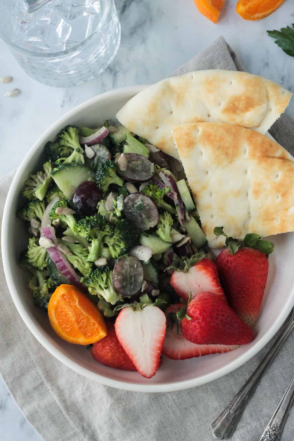 Broccoli salad in a white bowl with pita bread and fresh strawberries.