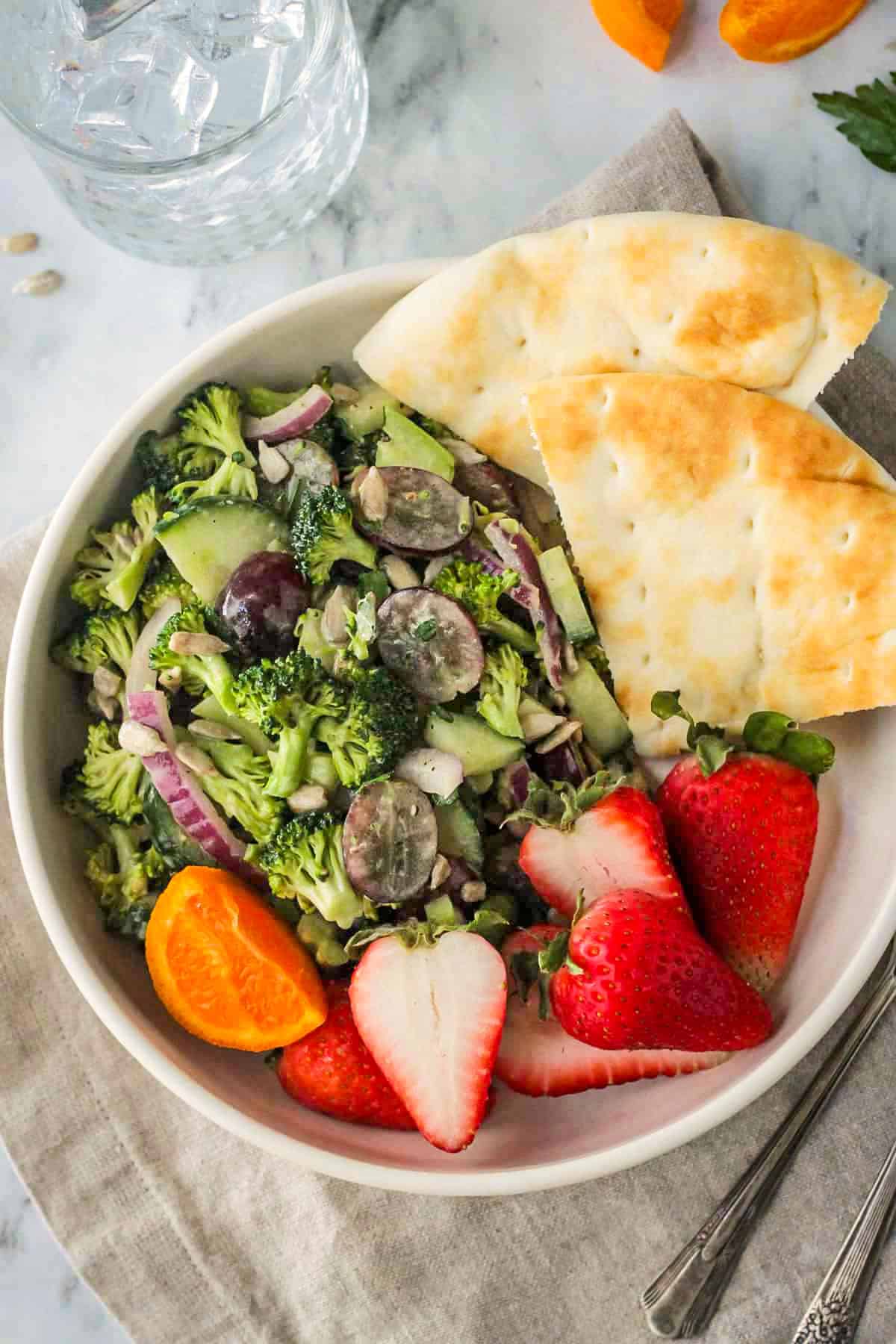 Tahini broccoli salad in a white bowl with pita bread and fresh strawberries.