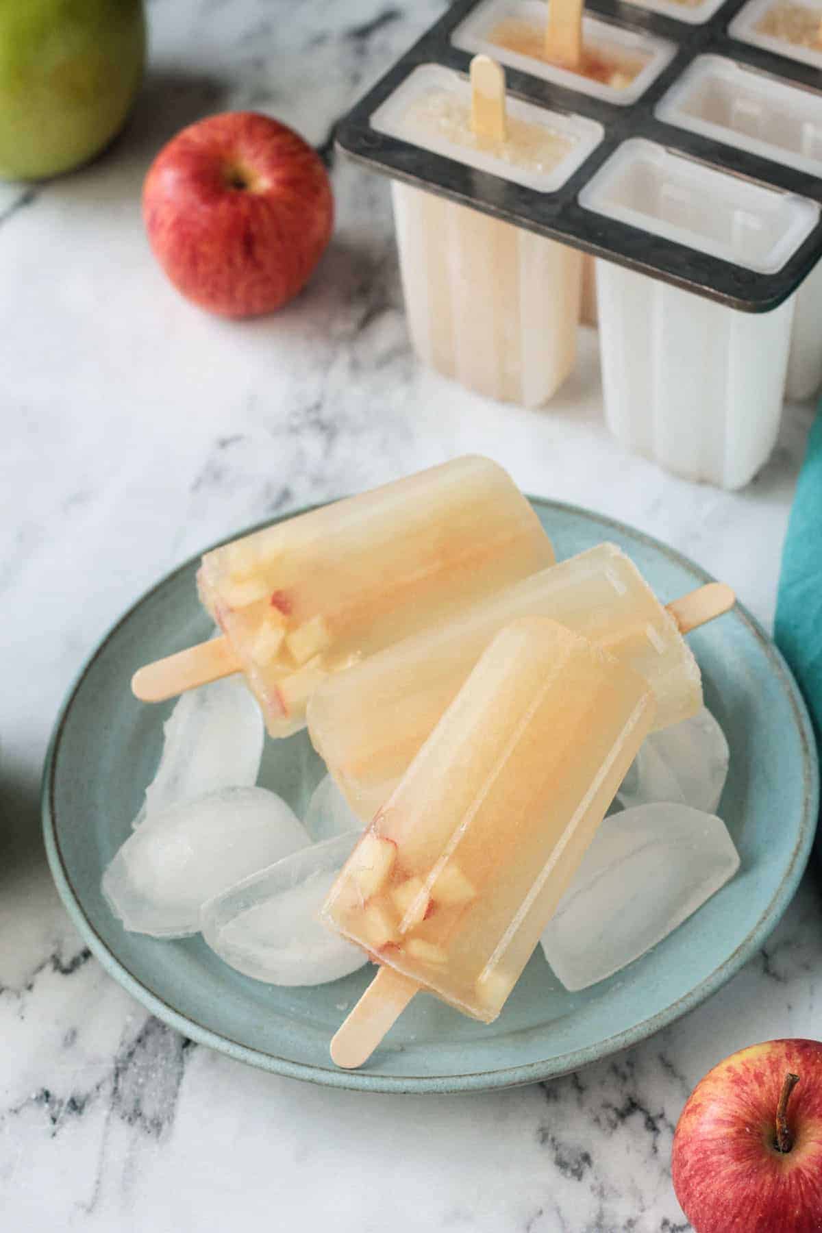 Three apple popsicles lying on ice cubes on a blue plate.