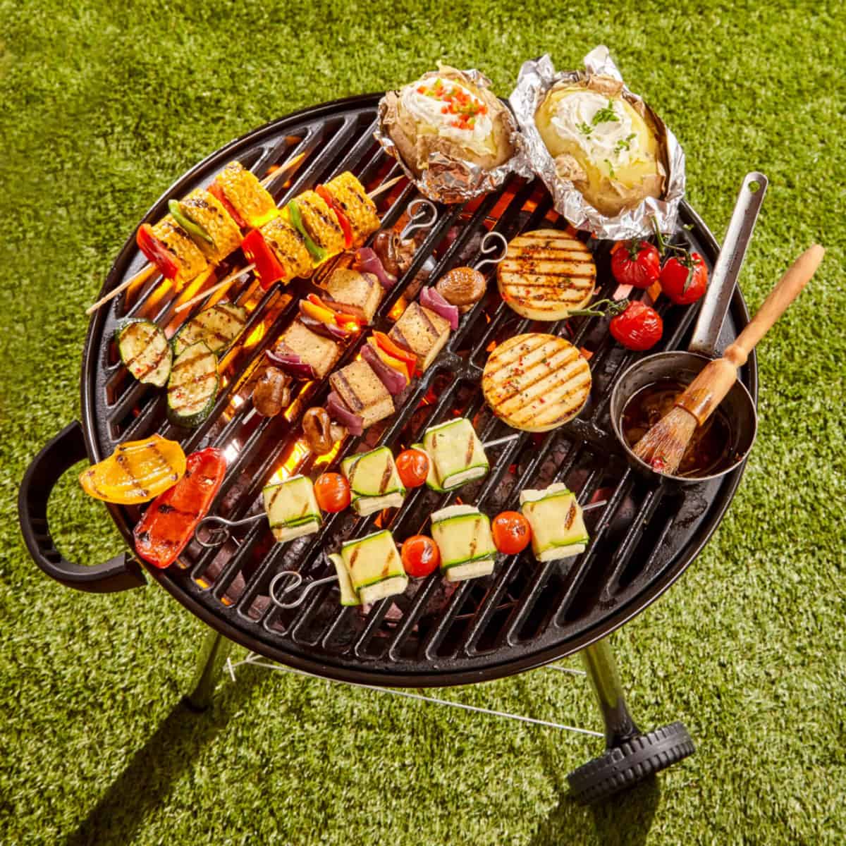Veggie kabobs on a charcoal grill with sauce and basting brush.