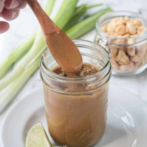 Peanut sauce dripping off of a wooden spatula in a glass jar.