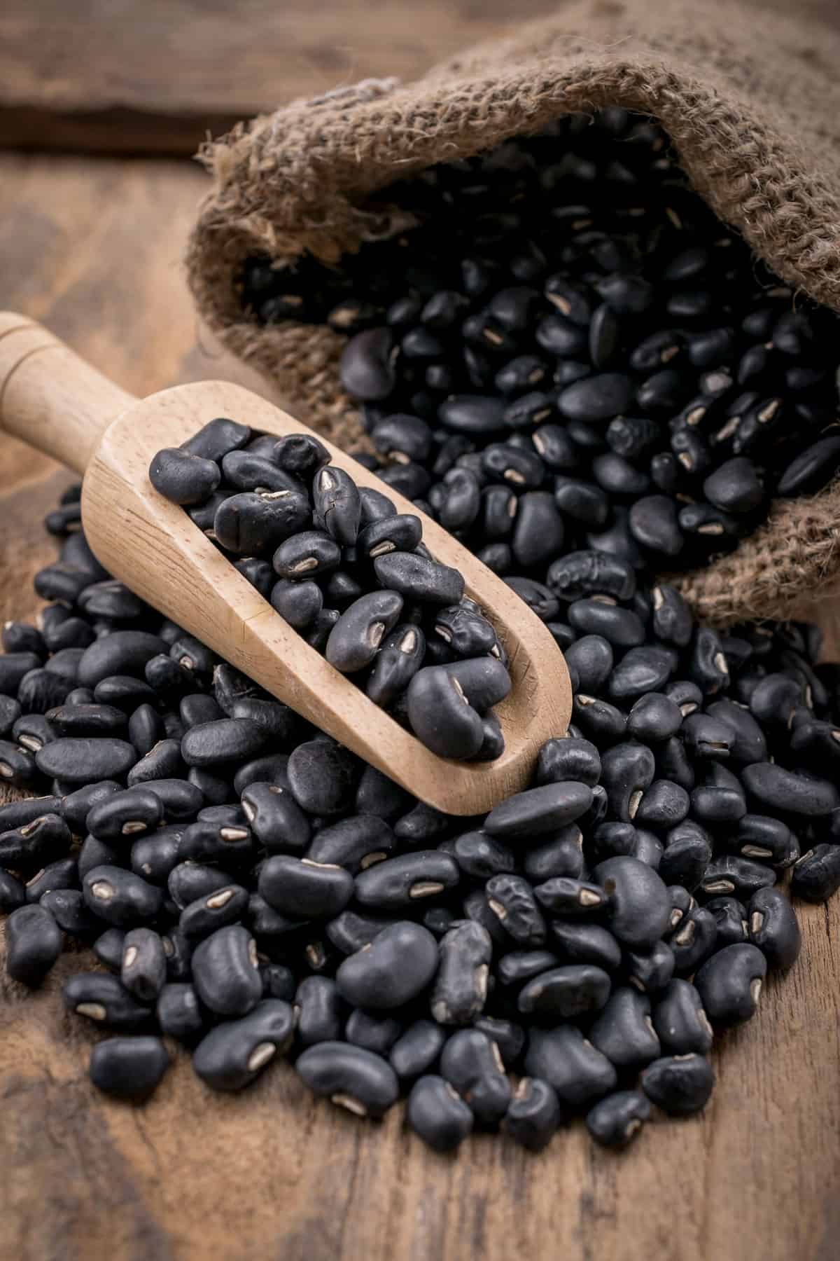 Black beans spilling out of a burlap sack onto a wooden table.