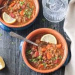 Metal spoon in a bowl of lentil quinoa soup with carrots and parsley.