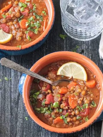 Metal spoon in a bowl of lentil quinoa soup with carrots and parsley.