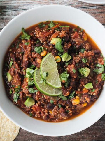 Bowl of black bean quinoa chili topped with diced avocado and two lime slices.