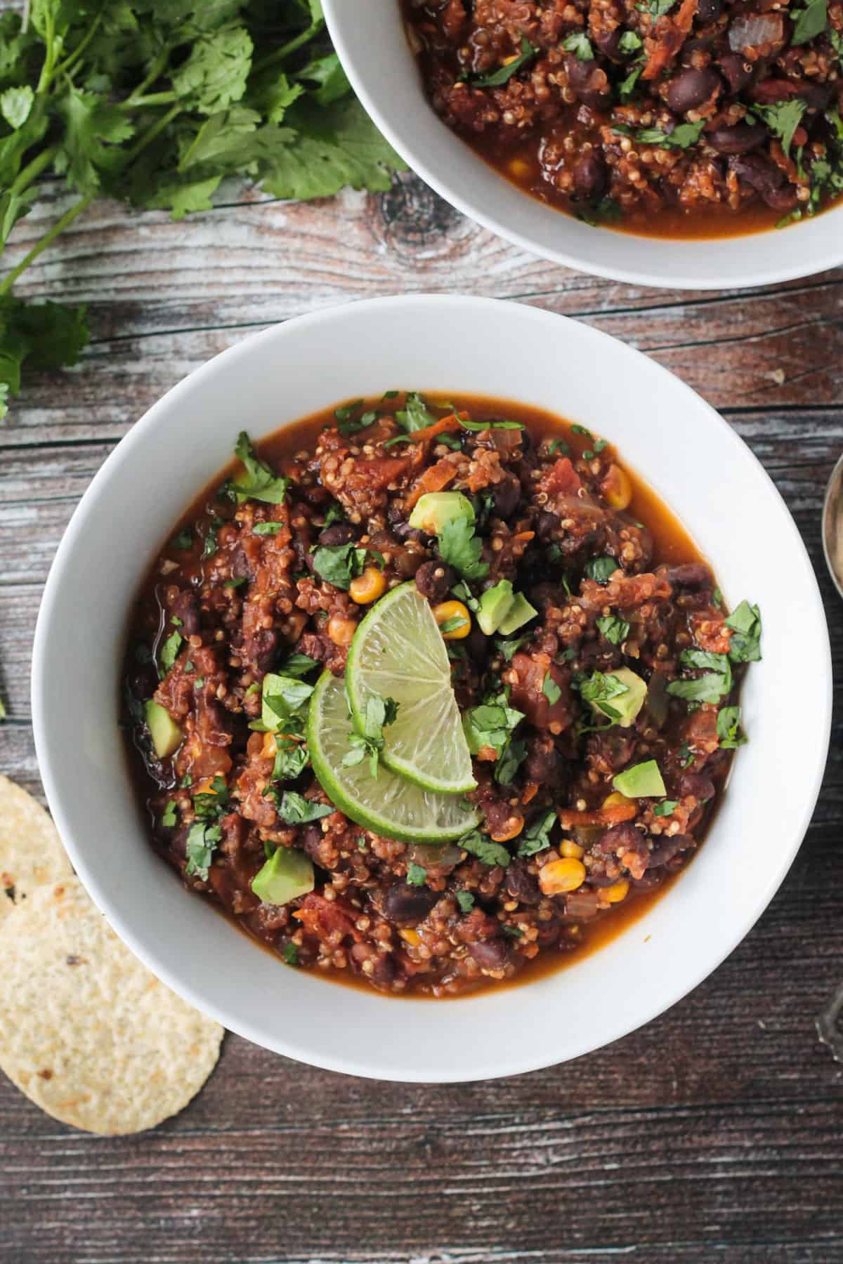 Bowl of black bean quinoa chili topped with diced avocado and two lime slices.