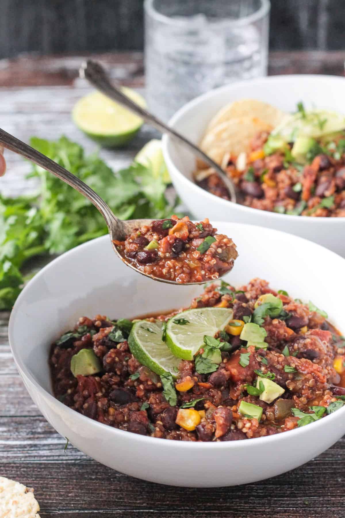 Spoonful of chili with black beans and quinoa being lifted out of a white bowl. 