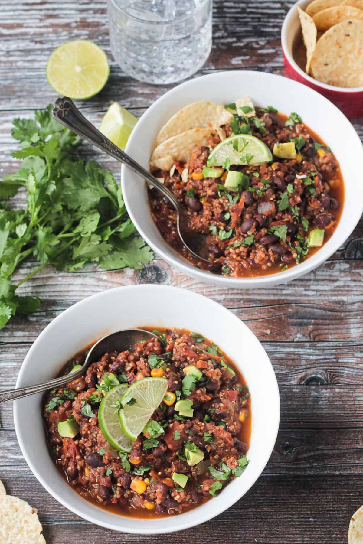Two white bowls of black bean quinoa chili with spoons in them.