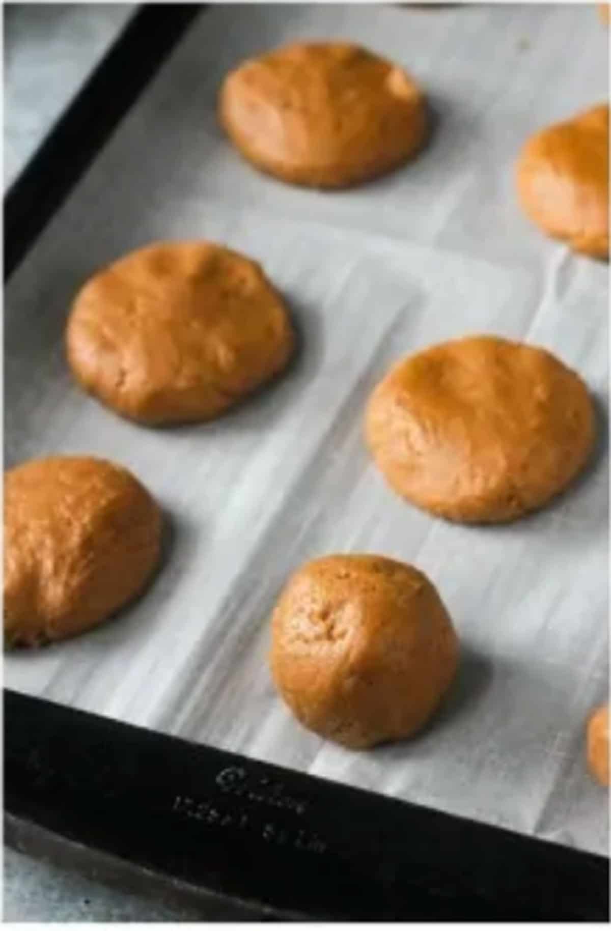Balls of cookie dough on a parchment lined cookie sheet.
