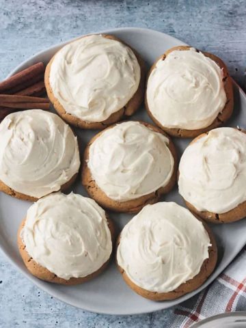 7 pumpkin cookies with white frosting on a plate.