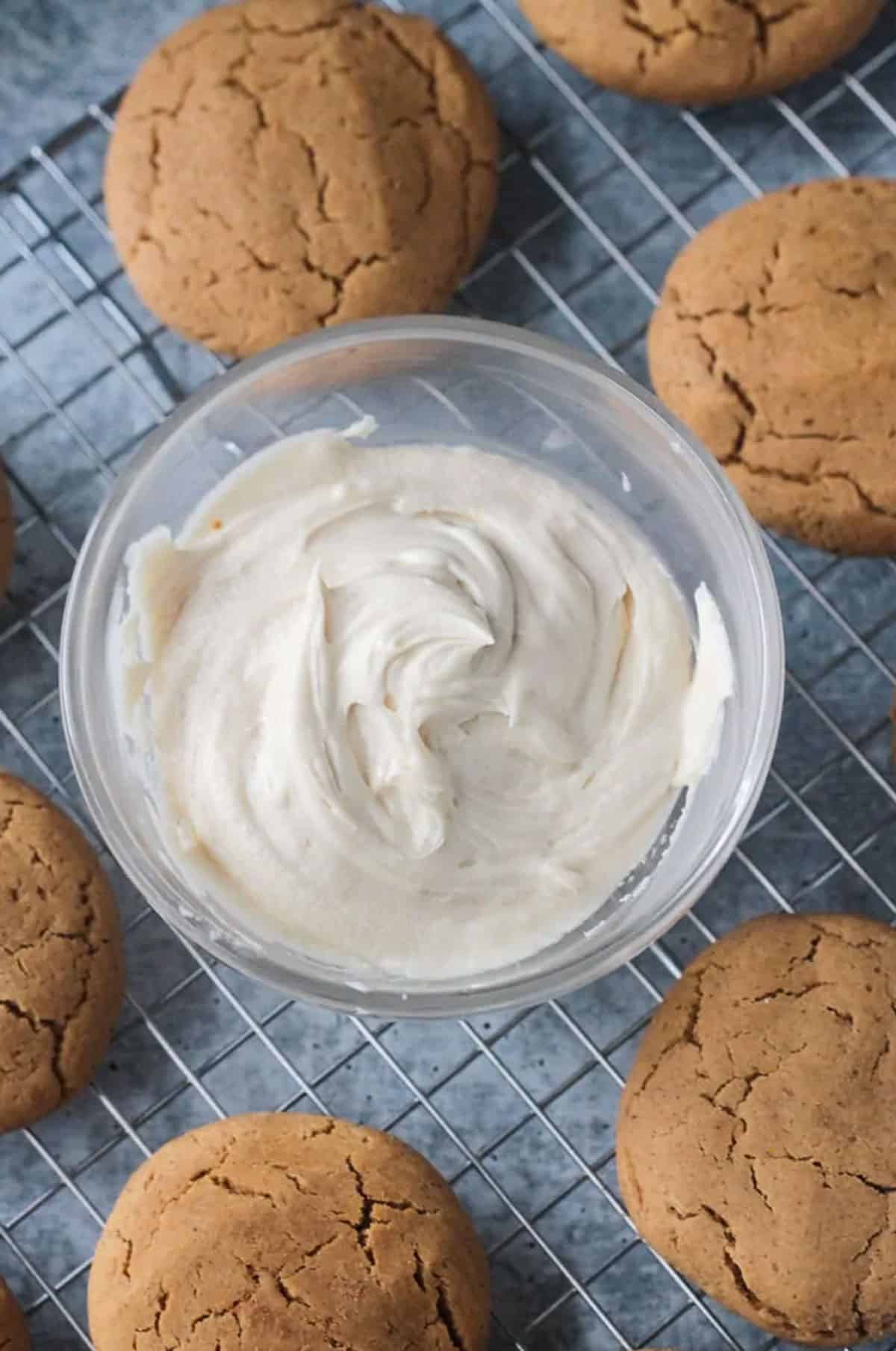 White maple frosting in a glass bowl surrounded by cookies.