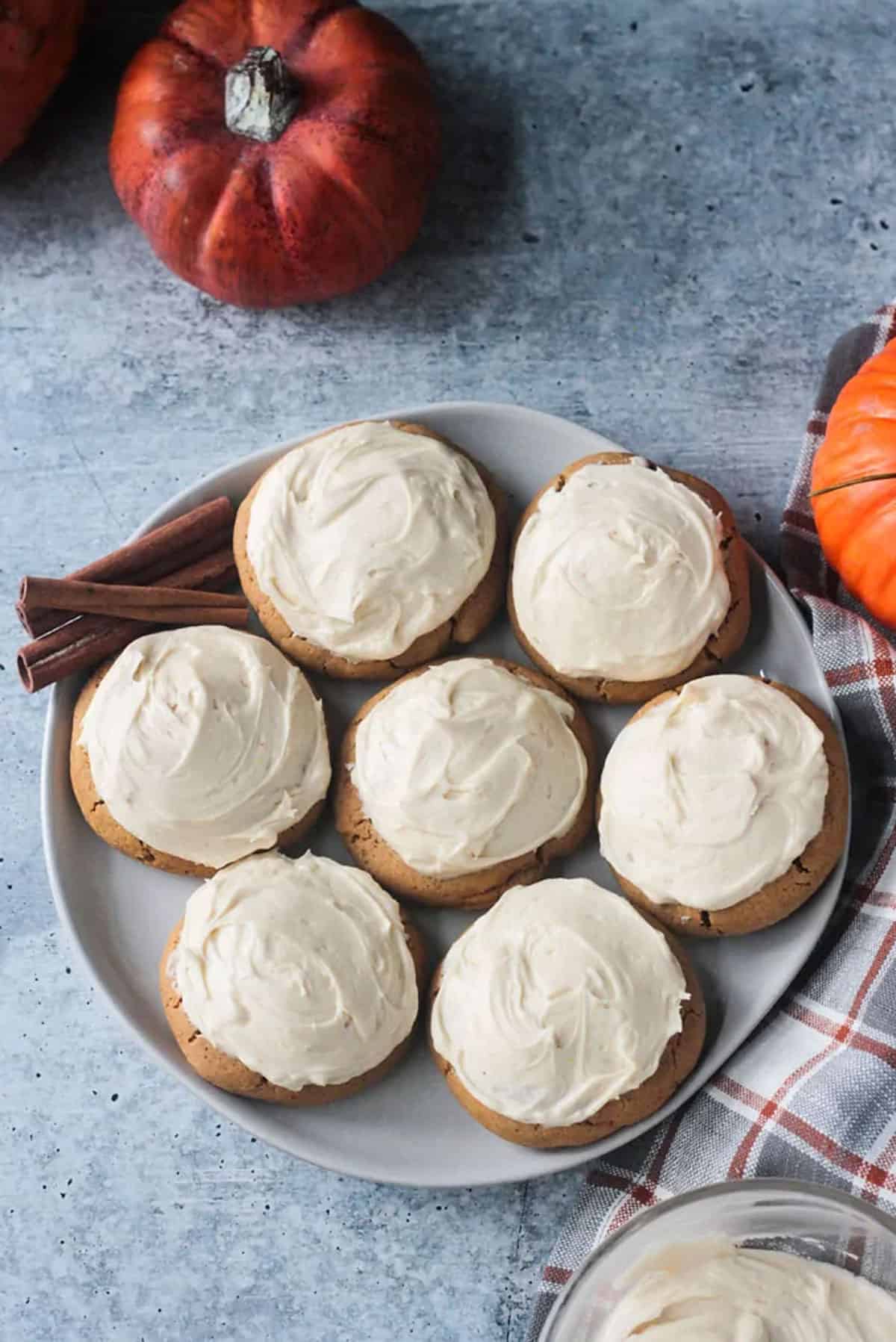 7 pumpkin cookies with white frosting on a plate w/ 3 cinnamon sticks.