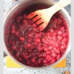 A wooden spoon in a pot of simmering cranberry sauce.