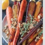 Close up of toasted walnuts and thyme sprigs on a plate of roasted rainbow carrots.