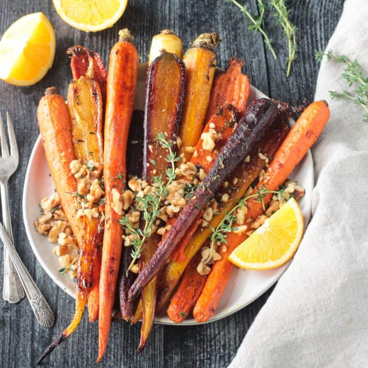 Plate of roasted rainbow carrots topped with walnuts and thyme leaves.