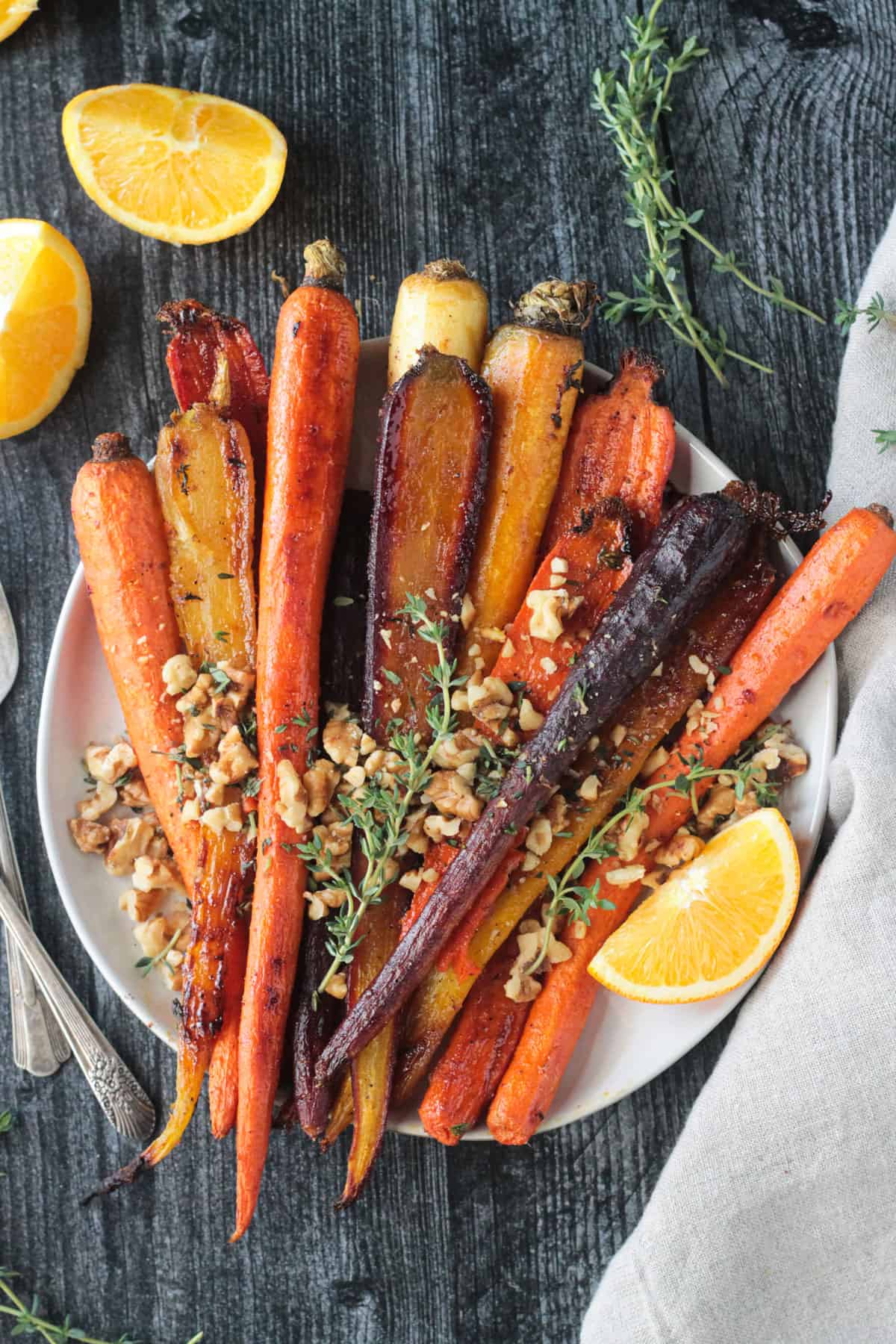 Plate of roasted rainbow carrots topped with walnuts and thyme leaves.