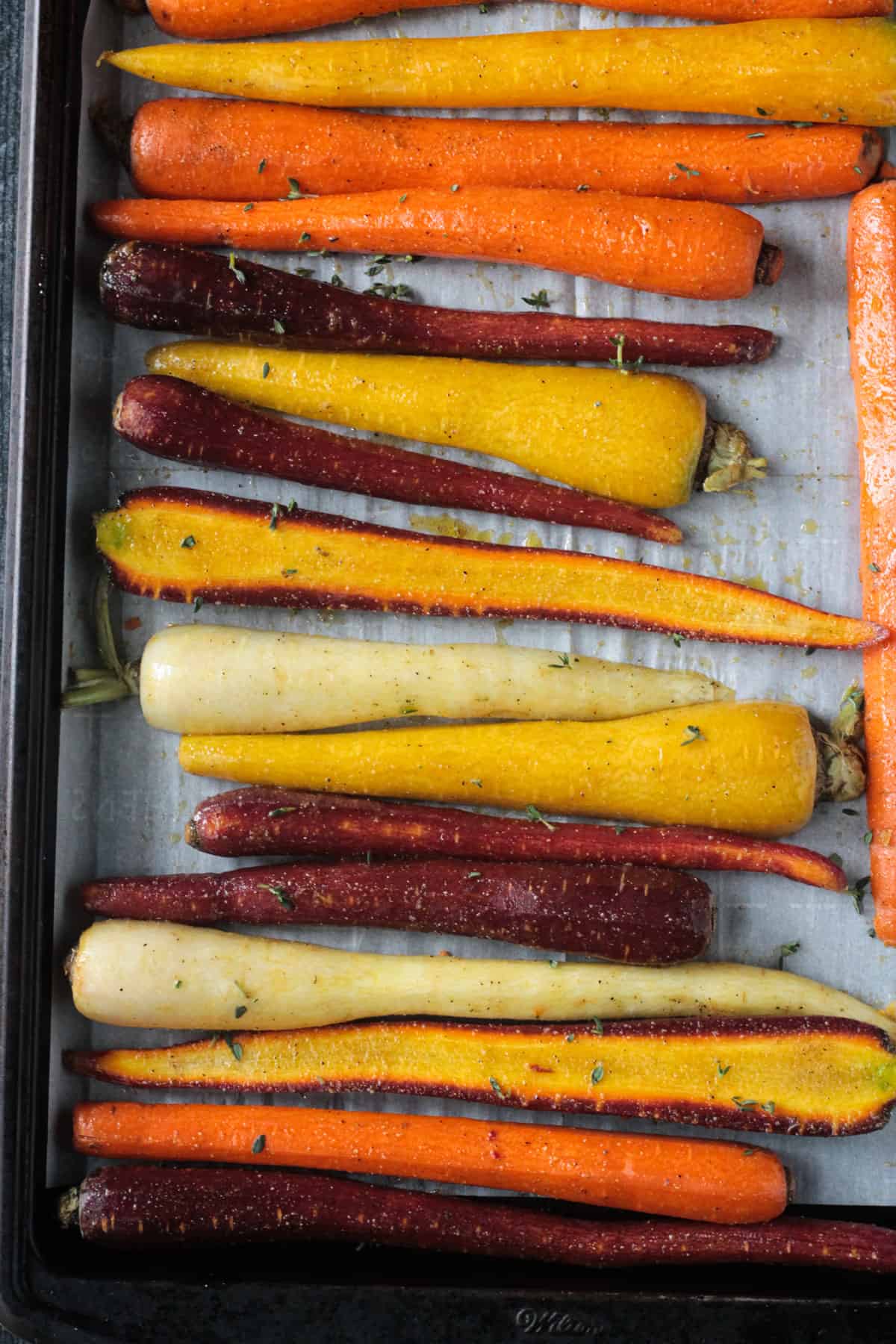 Roasted rainbow carrots on a parchment lined baking sheet.