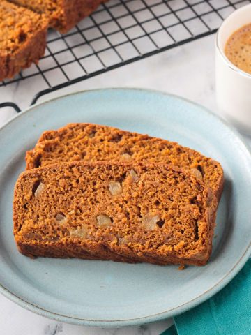 Two slices of vegan pumpkin bread on a blue plate next to a cup of coffee.