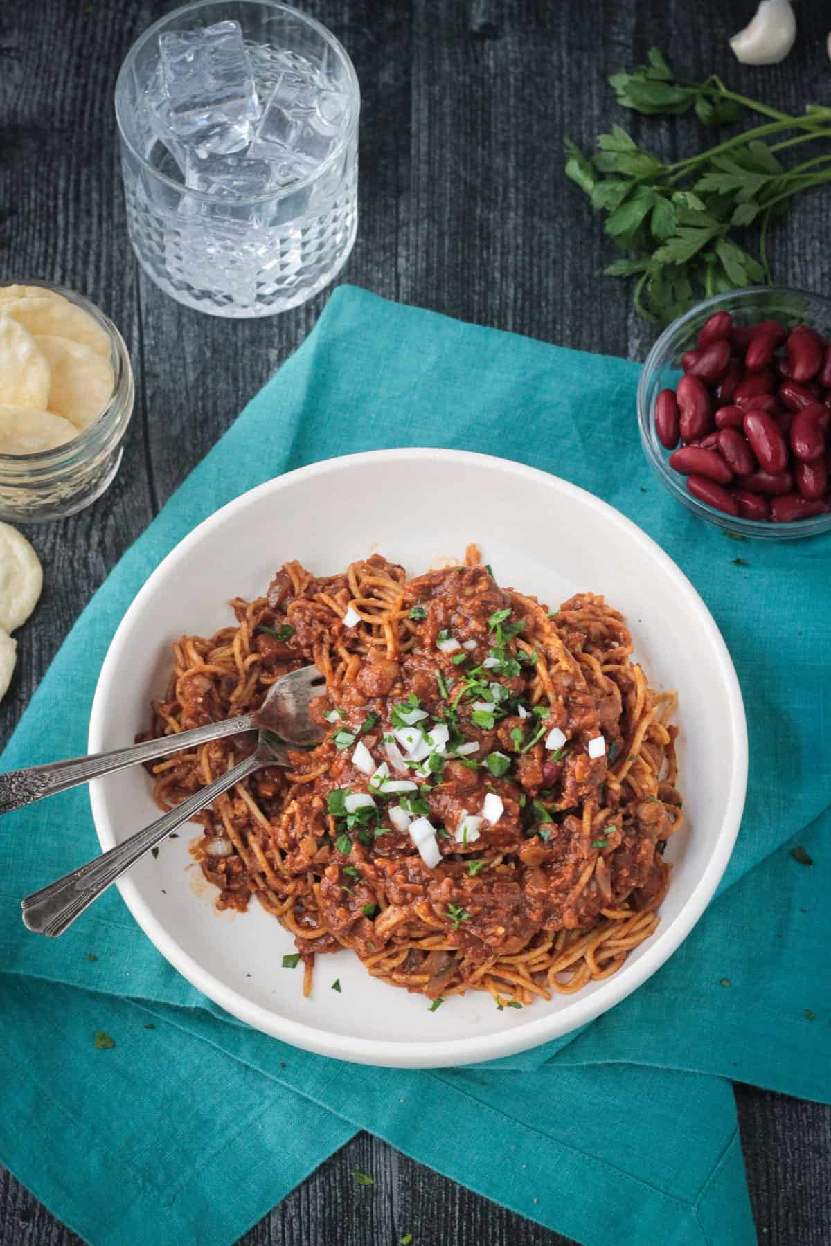 Two forks in chili sauced noodles in a handmade white flat bowl.