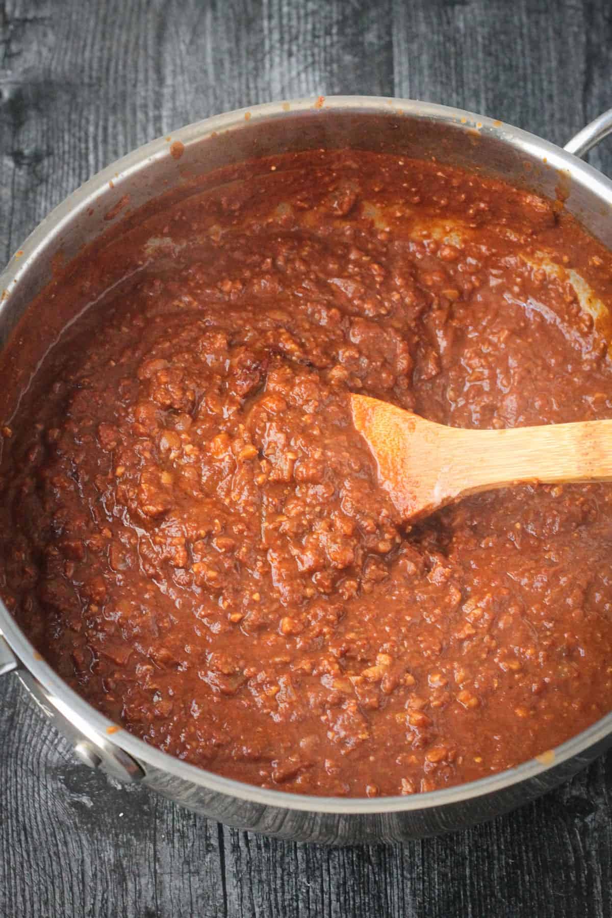 Wooden spoon stirring the finished thick sauce in a pot.