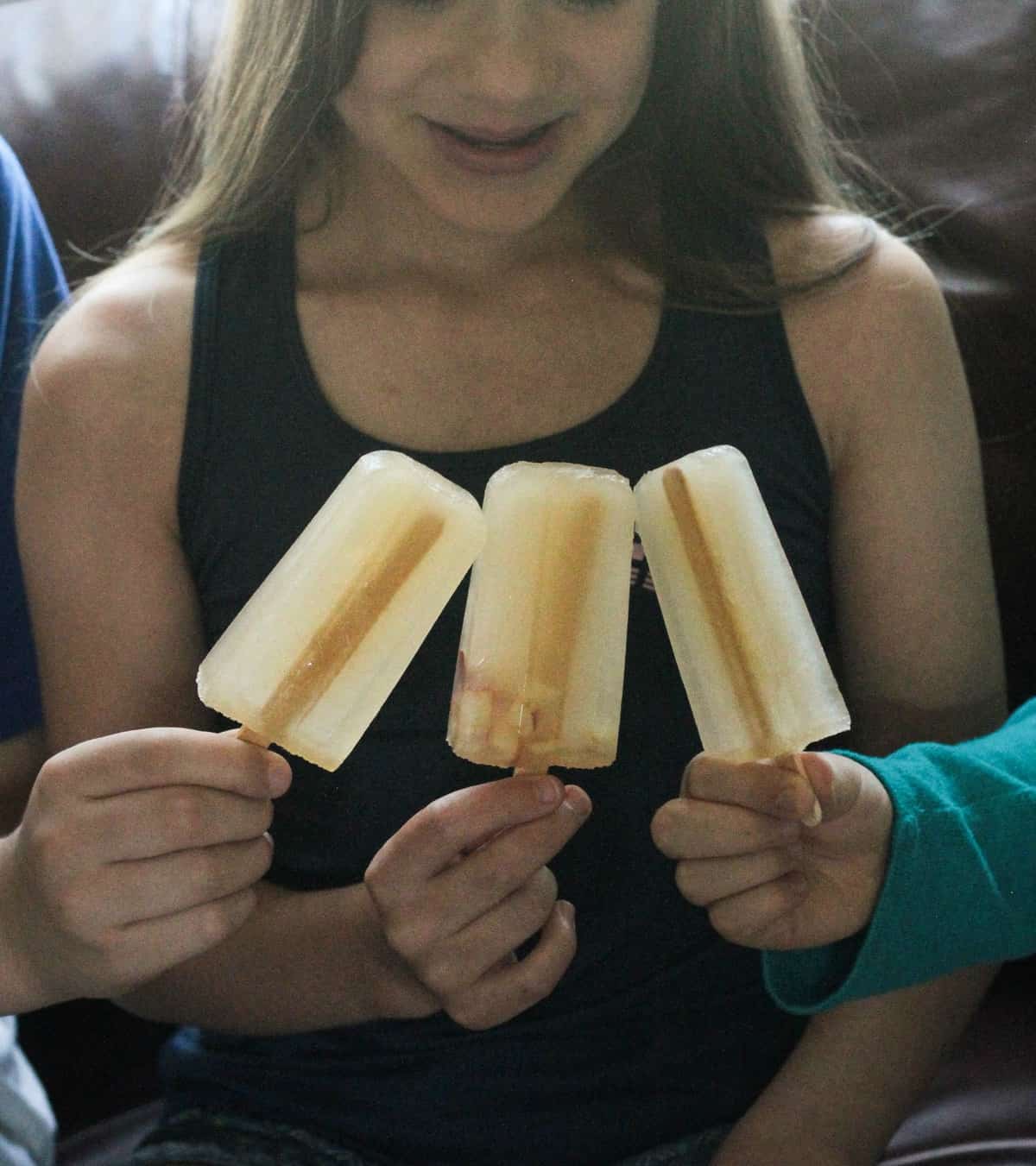 Three children's hands holding apple juice popsicles.