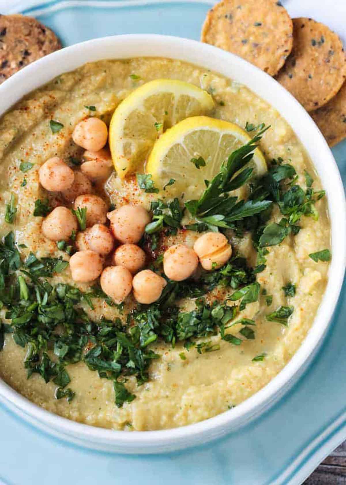 Close up of chickpeas and chopped parsley on top of a bowl of creamy hummus.