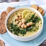 Hummus recipe without tahini garnished with chopped parsley and two lemon slices.