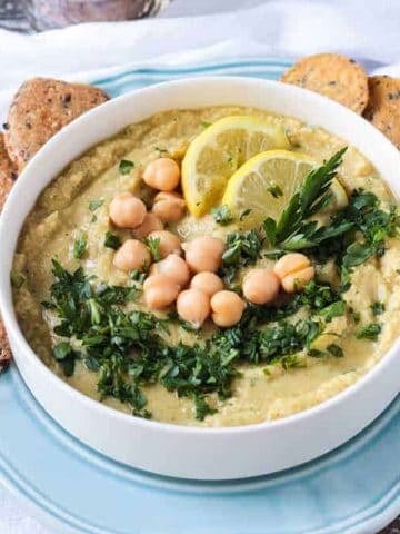 Hummus recipe without tahini garnished with chopped parsley and two lemon slices.