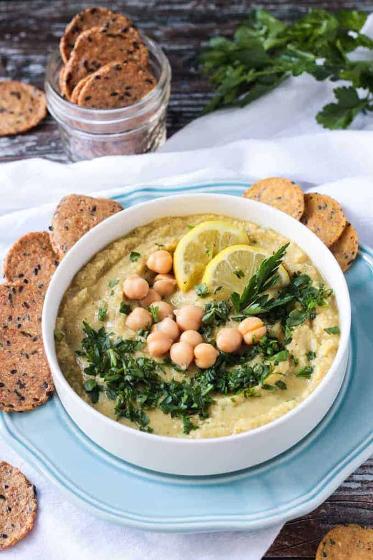 Hummus recipe without tahini garnished with chopped parsley and two lemon slices.