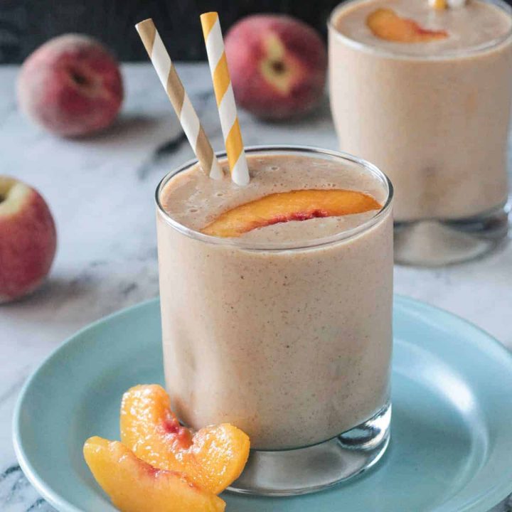 Two peach slices next to an almond butter smoothie on a blue plate.