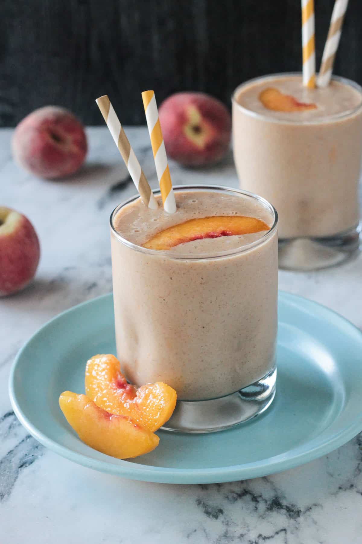 Two peach slices next to an almond butter smoothie in a glass on a blue plate.