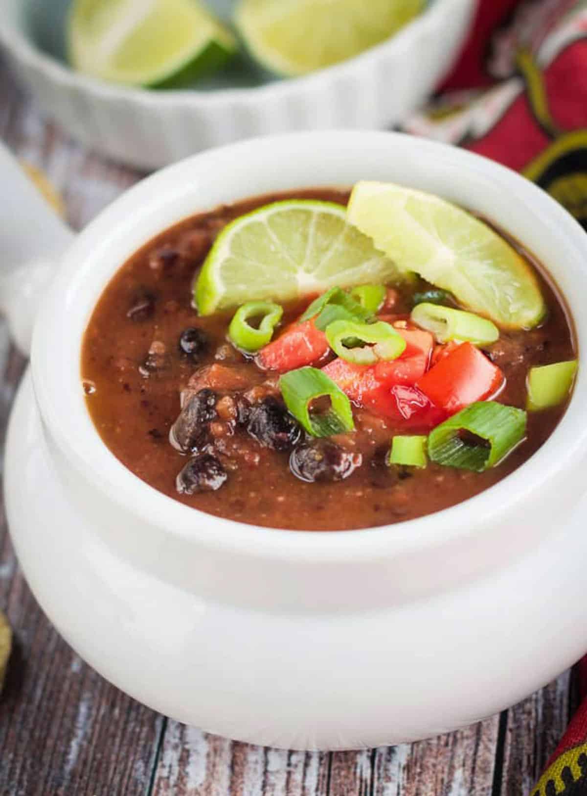 Close up of soup in a white bowl with toppings of lime and green onion.