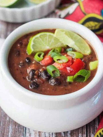 Bowl of black bean soup topped with diced tomatoes and two lime wedges.