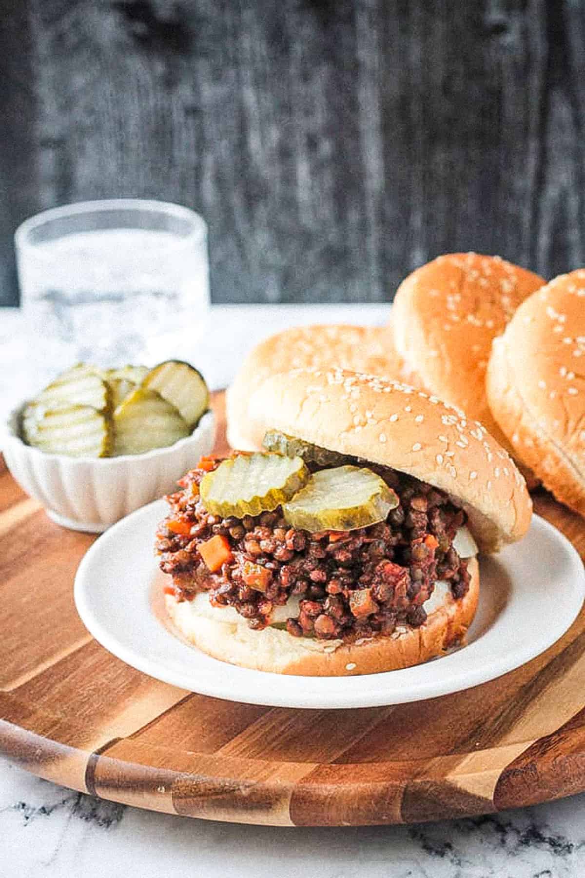 Saucy lentil veggie mixture with pickles and an offset sesame seed bun.