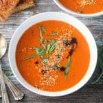 Bowl of tomato soup garnished with fresh basil, hemp seeds, and drizzle of balsamic vinegar.