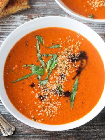 Bowl of tomato soup garnished with fresh basil, hemp seeds, and drizzle of balsamic vinegar.