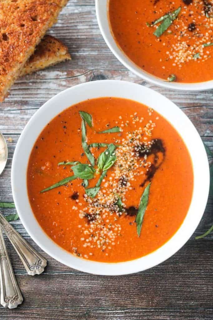 Bowl of tomato soup garnished with fresh basil, hemp seeds, and drizzle of balsamic vinegar.