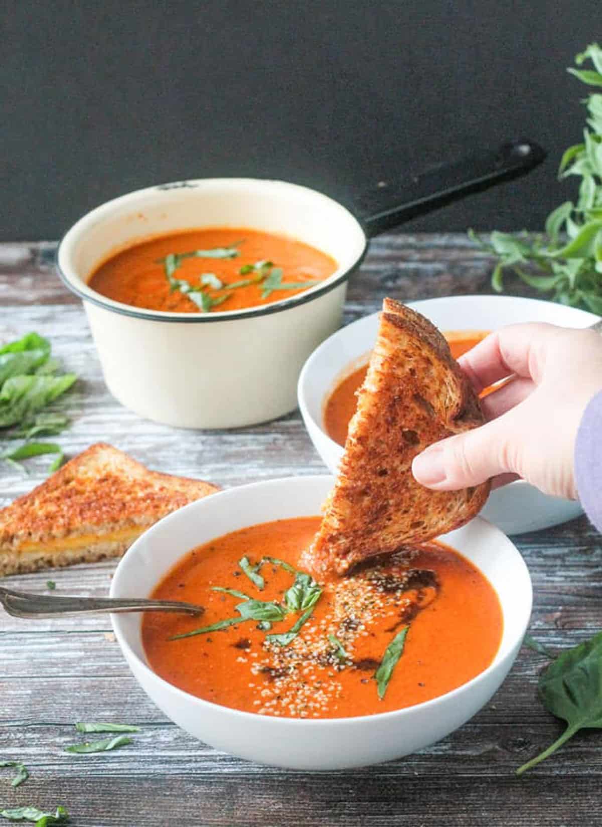 Half of a grilled cheese sandwich being dipped into a bowl of soup.