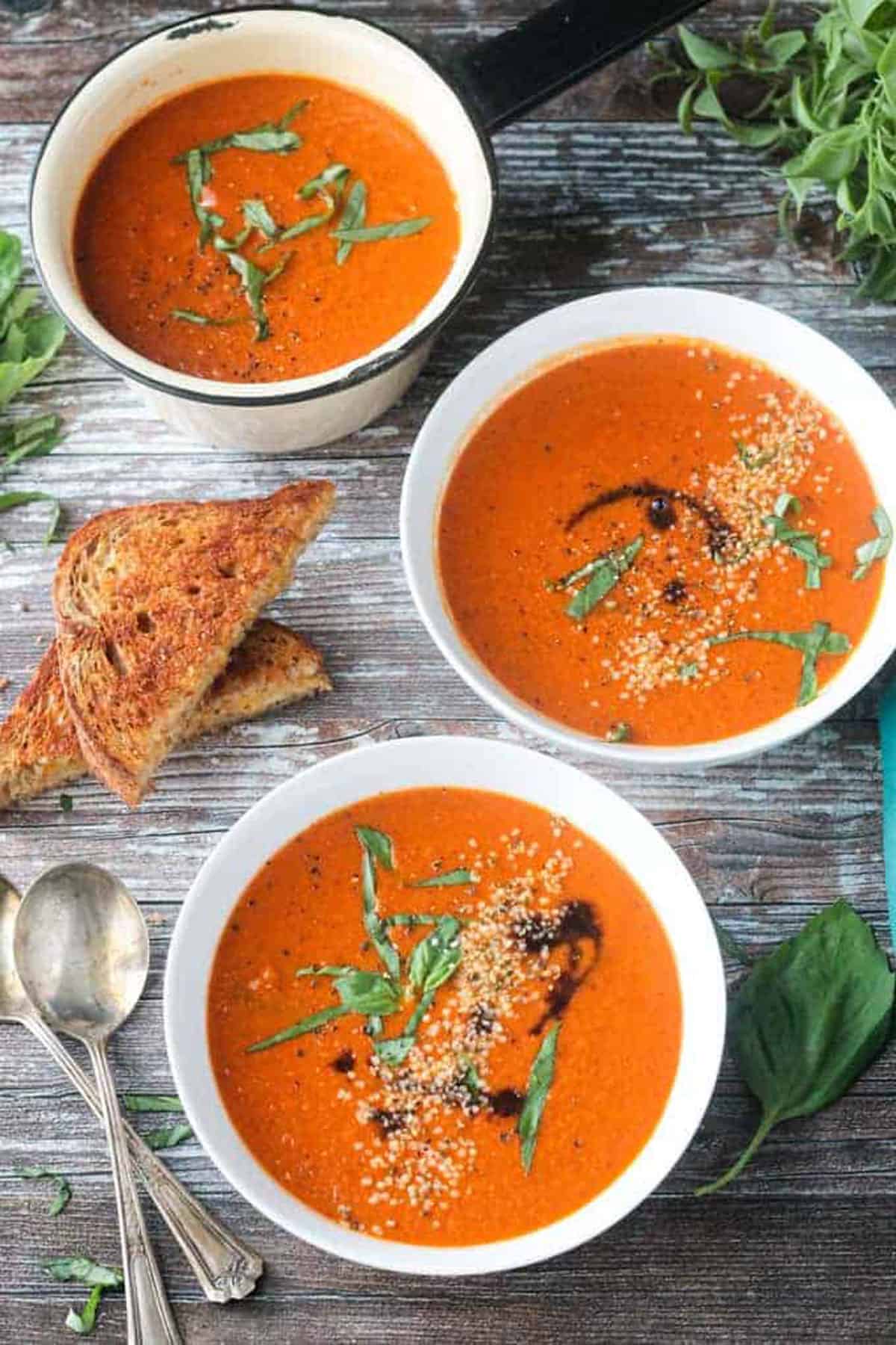 Two bowls of vegan tomato soup next to stacked grilled cheese sandwiches.