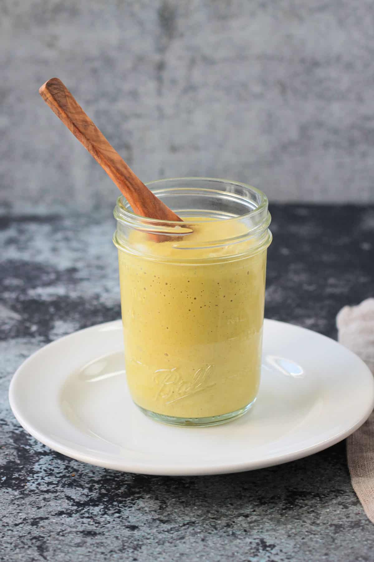 Cashew curry sauce in a glass jar with a wooden spoon.