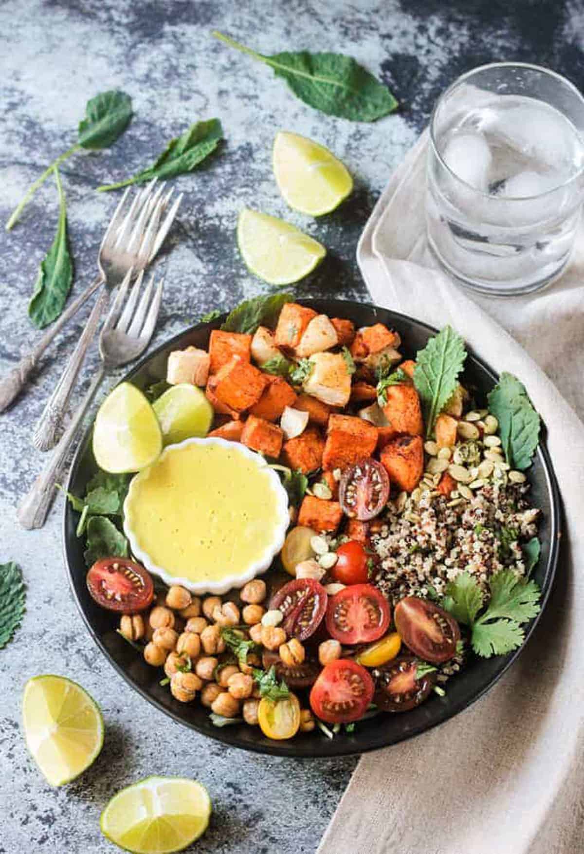 Sweet Potato Quinoa Buddha Bowl - Roasted vegetables, healthy plant protein, lots of texture, bursts of fresh flavor, and a creamy dairy free Cashew Curry Sauce to bring it all together. A delicious fall vegetarian meal suitable for any night of the week. Kid friendly and customizable. Vegan and gluten free! Three forks lie next to a Sweet Potato Quinoa Bowl with Cashew Curry Sauce.