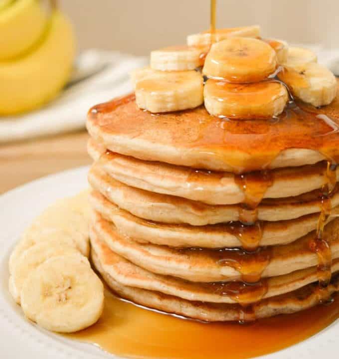 Stack of pancakes topped with banana slices and drizzle in maple syrup.