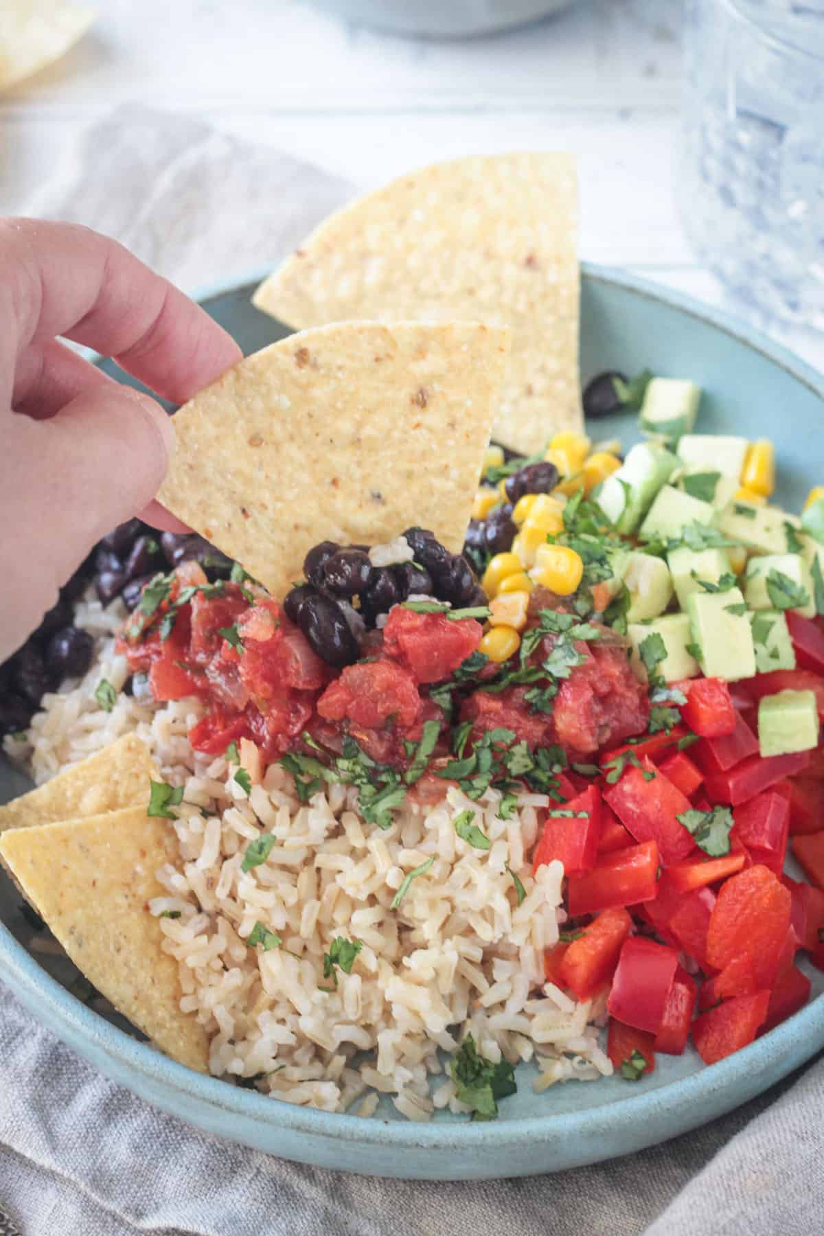 Ręczne nabieranie składników miski burrito za pomocą chipsów tortilla.