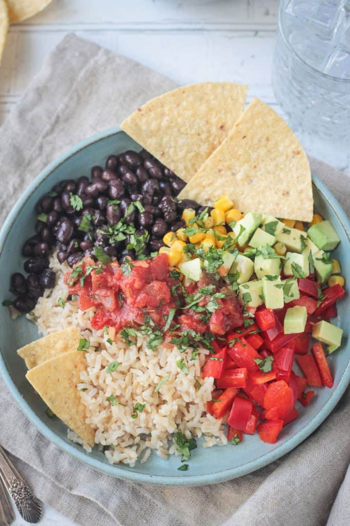 Two tortilla chips on the side of beans and rice topped with avocado and salsa.