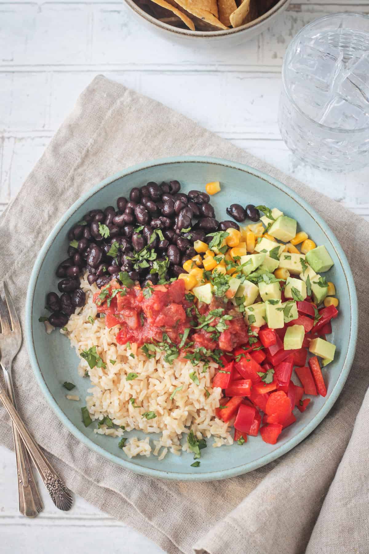 Vegan burrito bowl with rice, beans, corn, peppers, salsa, and avocado on a plate.