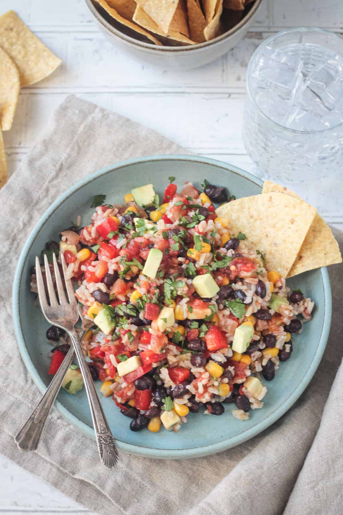 Rice, black beans, corn, diced red peppers, and avocado mixed together on a blue plate with a fork.