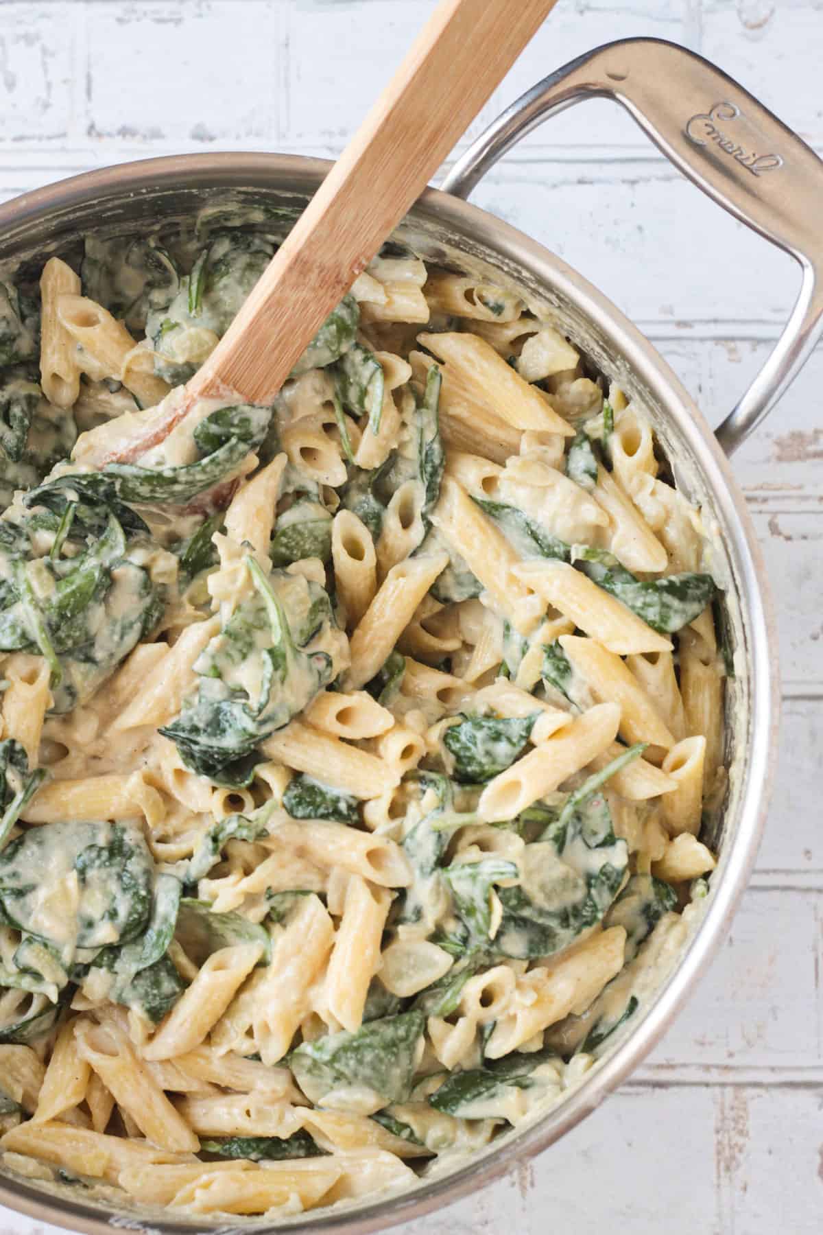 Close up of penne pasta, spinach, and artichokes in a creamy sauce.
