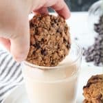 Adult hand dunking a cookie into a glass of milk.