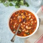 Metal spoon in a bowl of vegan minestrone soup.