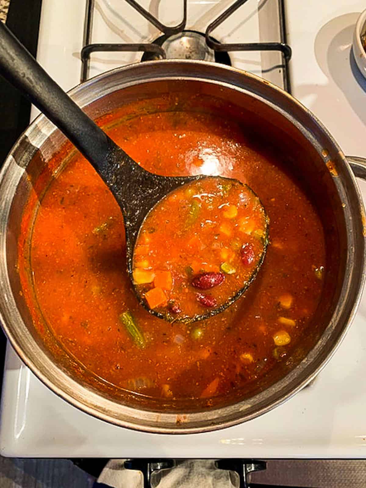 Ladle of minestrone soup coming out of the pot.